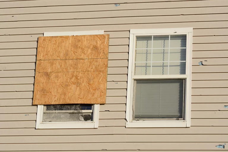hail damage restoration - photo of a home that has broken windows and cracked siding from a hail storm